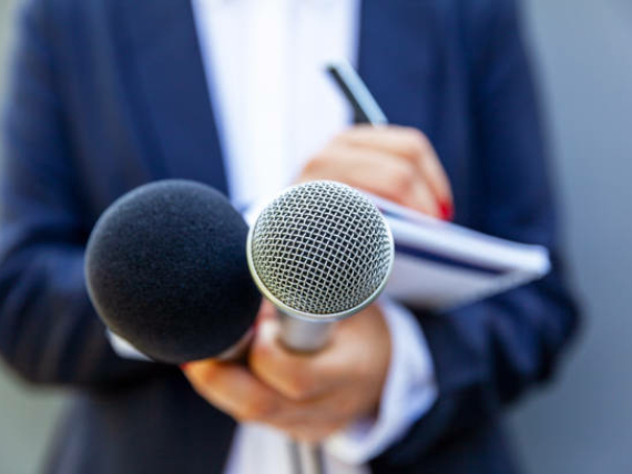 News reporter or TV journalist at press conference, holding microphone and writing notes